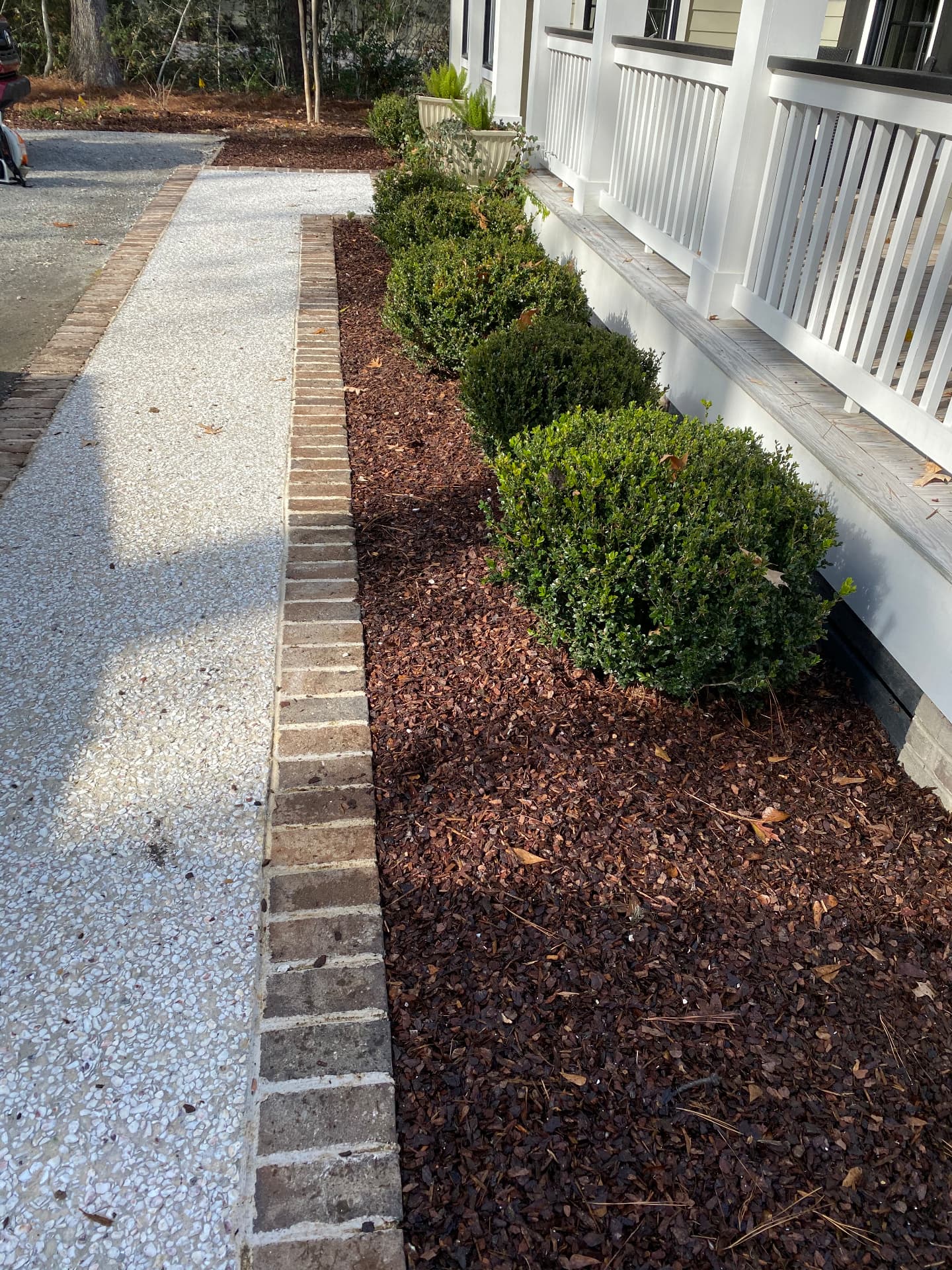 Fresh mulch bed with brick edging and trimmed boxwoods along a home's front porch